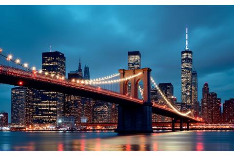 Iconic bridge in a bustling city at dusk, with lights reflecting on water.