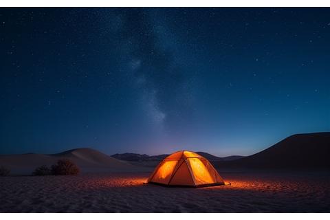 Desert camping under a starry night sky with a tent illuminated.